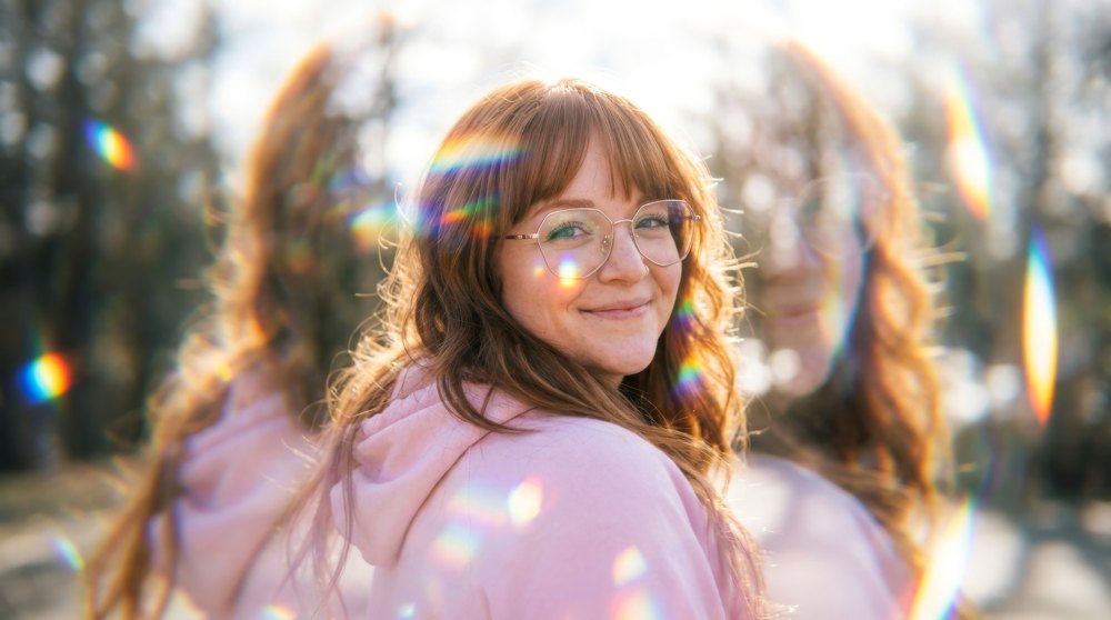 Amber smiling in a pink hoodie, with rainbow prism light around her